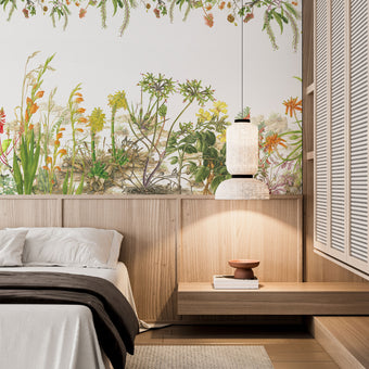 Botanical wallpaper mural featuring delicate South African flora and wildflowers in soft natural tones, with trailing greenery overhead and illustrated aloe, fynbos, and meadow plants across a light background. On a wall in a bedroom above the bed and wooden paneling. 