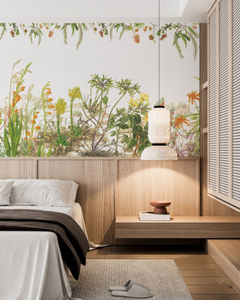 Botanical wallpaper mural featuring delicate South African flora and wildflowers in soft natural tones, with trailing greenery overhead and illustrated aloe, fynbos, and meadow plants across a light background. On a wall in a bedroom above the bed and wooden paneling. 