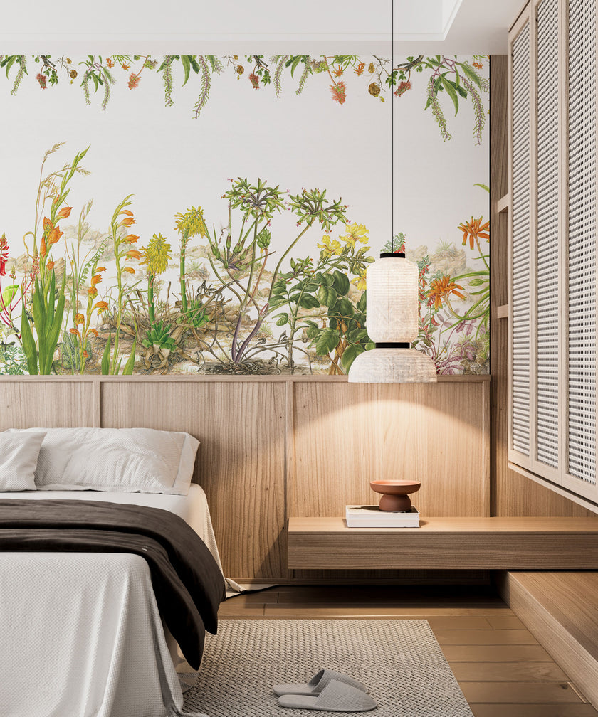 Botanical wallpaper mural featuring delicate South African flora and wildflowers in soft natural tones, with trailing greenery overhead and illustrated aloe, fynbos, and meadow plants across a light background. On a wall in a bedroom above the bed and wooden paneling. 