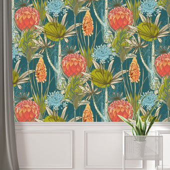 South African flower wallpaper with coral proteas, fynbos flowers, and layered foliage on a deep teal background. On wall above white paneling. 