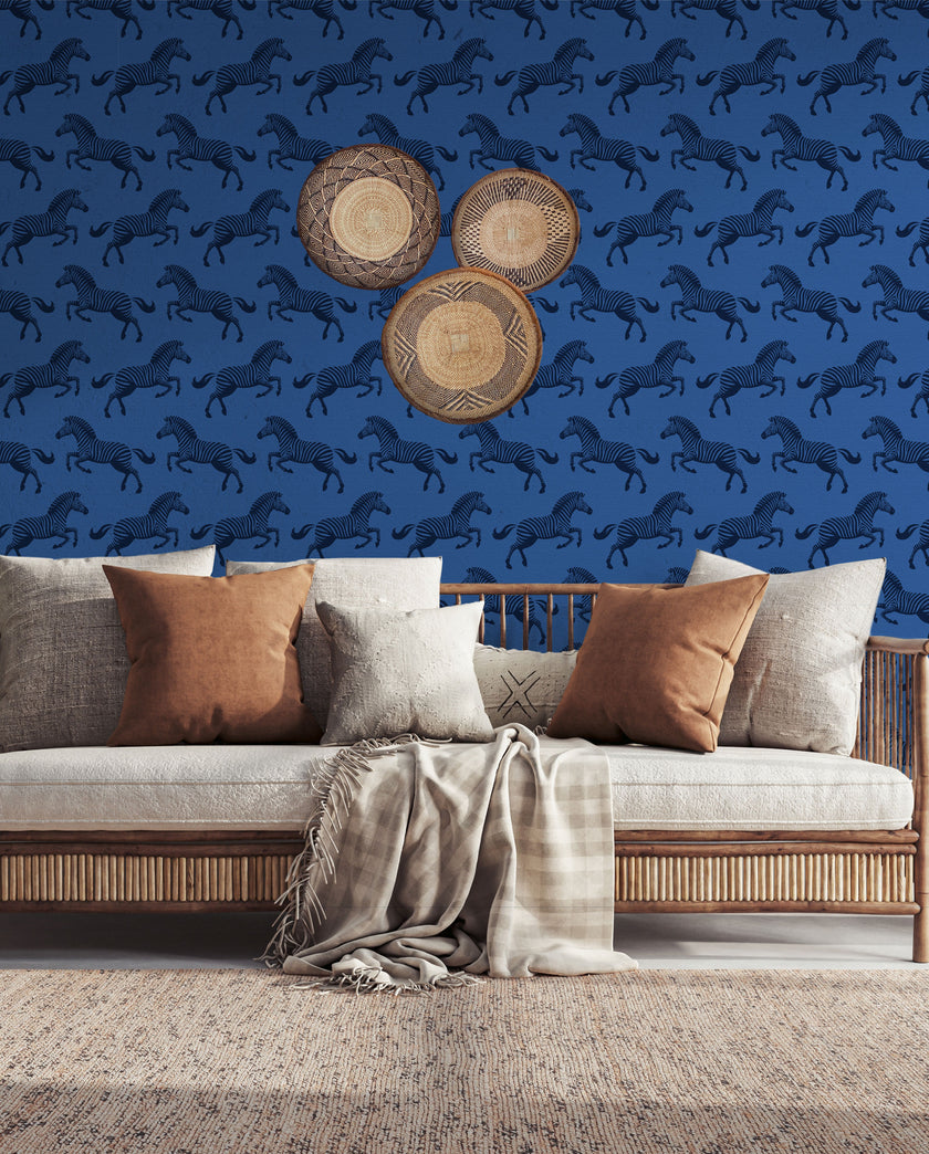 Repeating zebra wallpaper pattern featuring navy and royal blue zebras on a cobalt blue background. Wallpaper in a safari longe seating area, be hide the couch. 