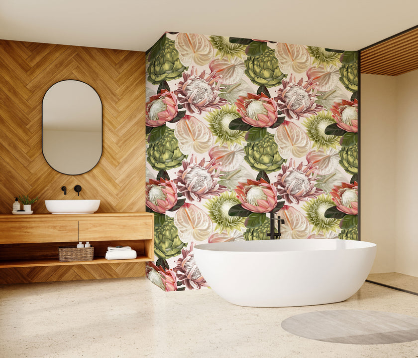 A modern bathroom interior featuring a freestanding white bathtub in front of a wall covered in a large-scale botanical print wallpaper with pink proteas and green leaves. To the left is a wood-look herringbone wall with an oval mirror and a matching wood vanity with a white sink.