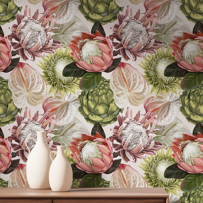 Botanical wallpaper with a seamless repeating pattern of hand painted blush pink proteas, cream anthuriums, and green foliage on a soft neutral background, styled behind a wooden cabinet with two white ceramic vases.
