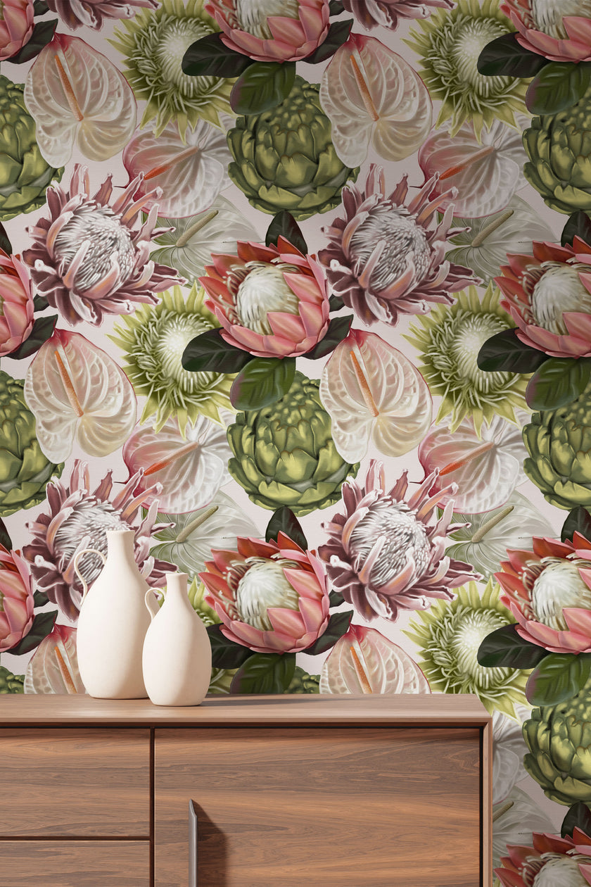 Botanical wallpaper with a seamless repeating pattern of hand painted blush pink proteas, cream anthuriums, and green foliage on a soft neutral background, styled behind a wooden cabinet with two white ceramic vases.
