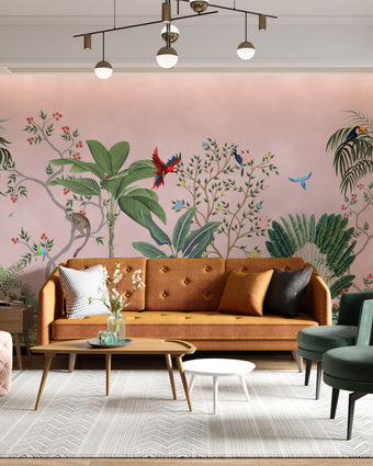 Blush pink tropical wallpaper with illustrated palms, birds, monkeys and delicate botanical details in a hand-painted chinoiserie style. On wall in a modern living room.