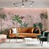 Blush pink tropical wallpaper with illustrated palms, birds, monkeys and delicate botanical details in a hand-painted chinoiserie style. On wall in a modern living room.