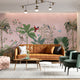 Blush pink tropical wallpaper with illustrated palms, birds, monkeys and delicate botanical details in a hand-painted chinoiserie style. On wall in a modern living room.