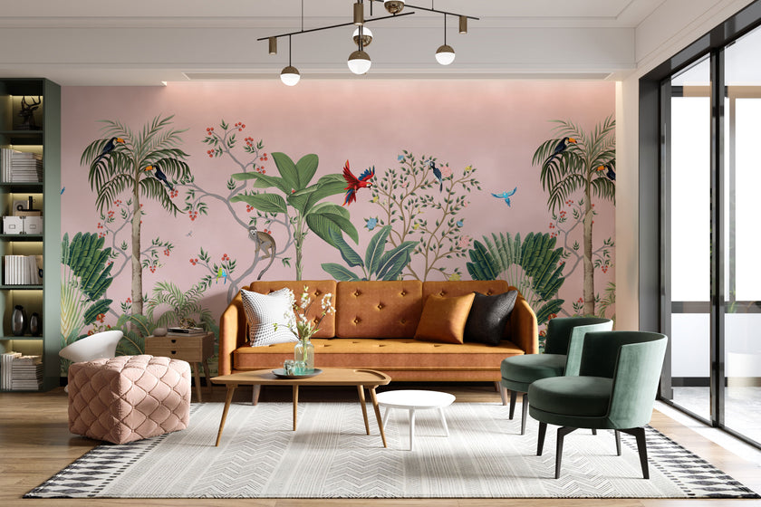 Blush pink tropical wallpaper with illustrated palms, birds, monkeys and delicate botanical details in a hand-painted chinoiserie style. On wall in a modern living room.