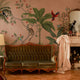 Blush pink tropical wallpaper with illustrated palms, birds, monkeys and delicate botanical details in a hand-painted chinoiserie style. On wall in a vintage living room. 