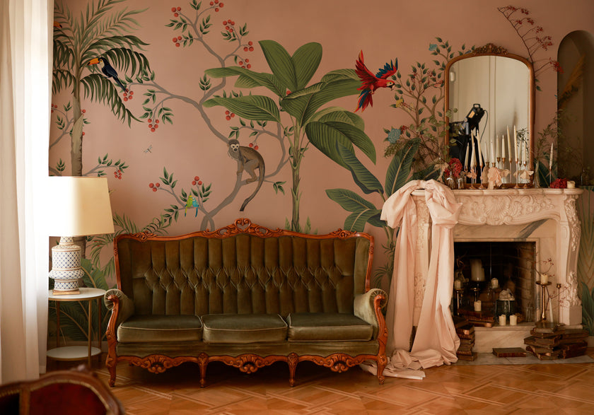 Blush pink tropical wallpaper with illustrated palms, birds, monkeys and delicate botanical details in a hand-painted chinoiserie style. On wall in a vintage living room. 