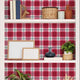 Playful pink tartan wallpaper with layered blush and red tones in a soft check design. Wallpaper behind shelves. 
