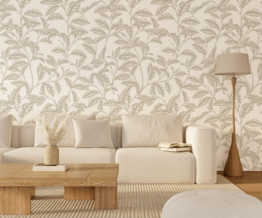 A styled living room scene featuring a cream coloured sofa against a wall with white botanical wallpaper featuring finely illustrated taupe camellia branches and delicate leaves. There is a wooden coffee table, a floor lamp, and a light rug.

