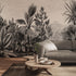 A large scale botanical wall mural featuring detailed black and white palm and tropical foliage, shown behind a grey sofa in a modern living room setting.