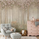 Children's woodland mural featuring a deer in a misty forest with wildflowers and flowering trees in soft blush and neutral tones, creating a dreamy nursery setting. In the room there is a light grey armchair, pink dresser, and other decorative items.
