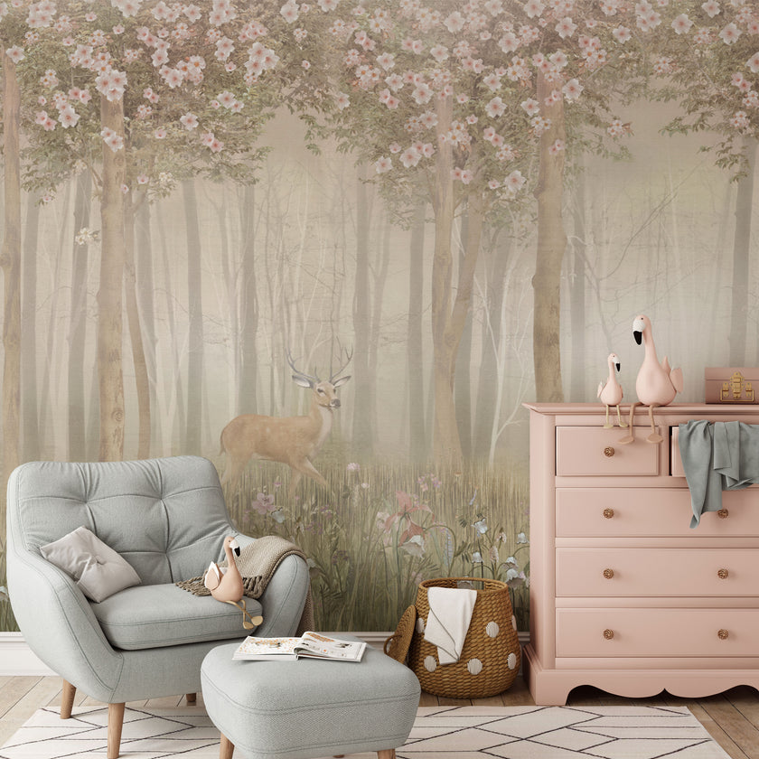 Children's woodland mural featuring a deer in a misty forest with wildflowers and flowering trees in soft blush and neutral tones, creating a dreamy nursery setting. In the room there is a light grey armchair, pink dresser, and other decorative items.
