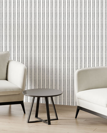 Two modern off white armchairs with black legs and a small round black side table, arranged in a minimalist room with potted plants and Navy and sage green striped wallpaper with organic dashes on a white background.