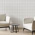 Two modern off white armchairs with black legs and a small round black side table, arranged in a minimalist room with potted plants and Navy and sage green striped wallpaper with organic dashes on a white background.