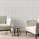 Two modern off white armchairs with black legs and a small round black side table, arranged in a minimalist room with potted plants and Navy and sage green striped wallpaper with organic dashes on a white background.