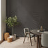 A styled interior corner featuring a charcoal grey botanical mural featuring oversized layered fern fronds on a textured grey background. With light wood flooring, a potted olive tree, woven baskets, and a round wooden dining table with grey upholstered chairs.