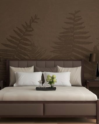 Chocolate brown botanical mural featuring oversized layered fern fronds on a textured brown background. On a wall behind a bed in brown colours with dark wood side tables. 