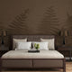 Chocolate brown botanical mural featuring oversized layered fern fronds on a textured brown background. On a wall behind a bed in brown colours with dark wood side tables. 