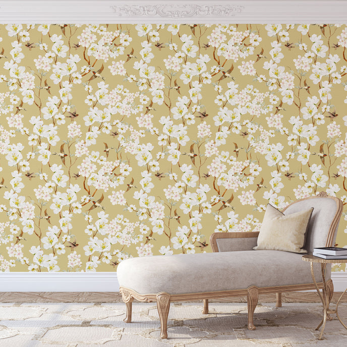Vintage inspired wallpaper featuring white and blush blossom flowers, winding branches, and swallows in flight on a warm golden-beige background.
