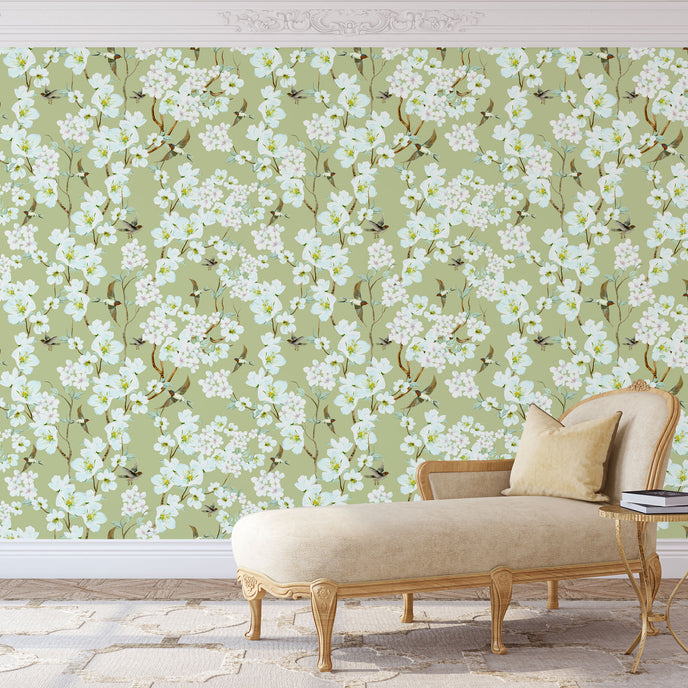 Chinoiserie inspired wallpaper featuring delicate white blossom flowers, flowering branches, and swallows in flight on a soft sage green background.