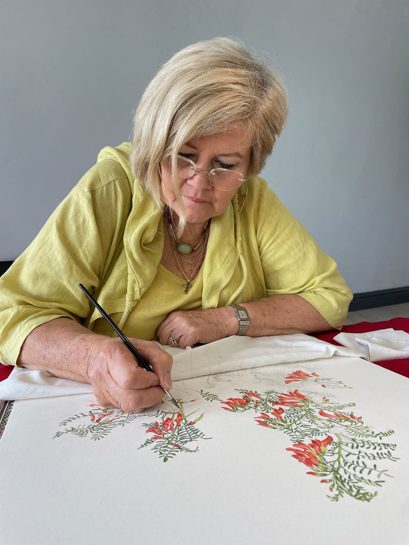 South African botanical artist Gillian Condy painting an illustration of the Sutherlandia frutescens plant, featuring delicate leaves and vibrant orange-red flowers in a detailed naturalistic style.