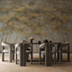 Forest mural featuring golden woodland trees with softly textured foliage against a smoky grey background, creating a warm and atmospheric nature inspired scene. On a wall behind a dinning table with dark furniture. 
