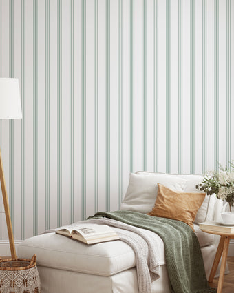 Classic green pinstripe wallpaper with fine vertical stripes, inspired by traditional country house interiors and timeless textile patterns. On lounge/seating area wall, behind couch. 