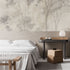 Neutral woodland wallpaper with soft ivory and taupe trees in a misty forest landscape. In a bedroom behind the beds headboard. 
