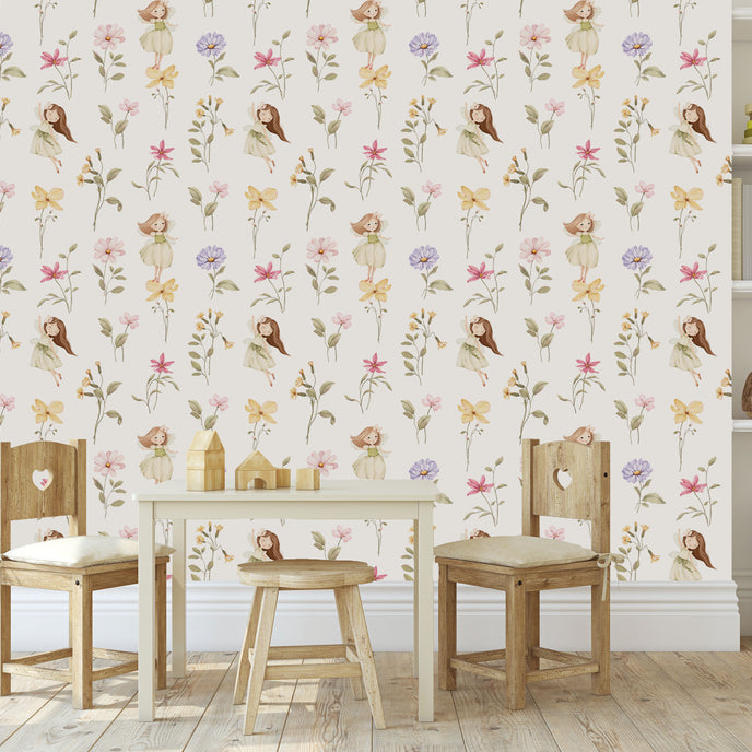 A styled children's playroom featuring a Whimsical little fairy wallpaper with delicate pink, lilac and yellow wildflowers and soft green foliage. In front of the wall is a small wooden table, two wooden chairs with cream cushions, and a small stool.