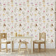A styled children's playroom featuring a Whimsical little fairy wallpaper with delicate pink, lilac and yellow wildflowers and soft green foliage. In front of the wall is a small wooden table, two wooden chairs with cream cushions, and a small stool.