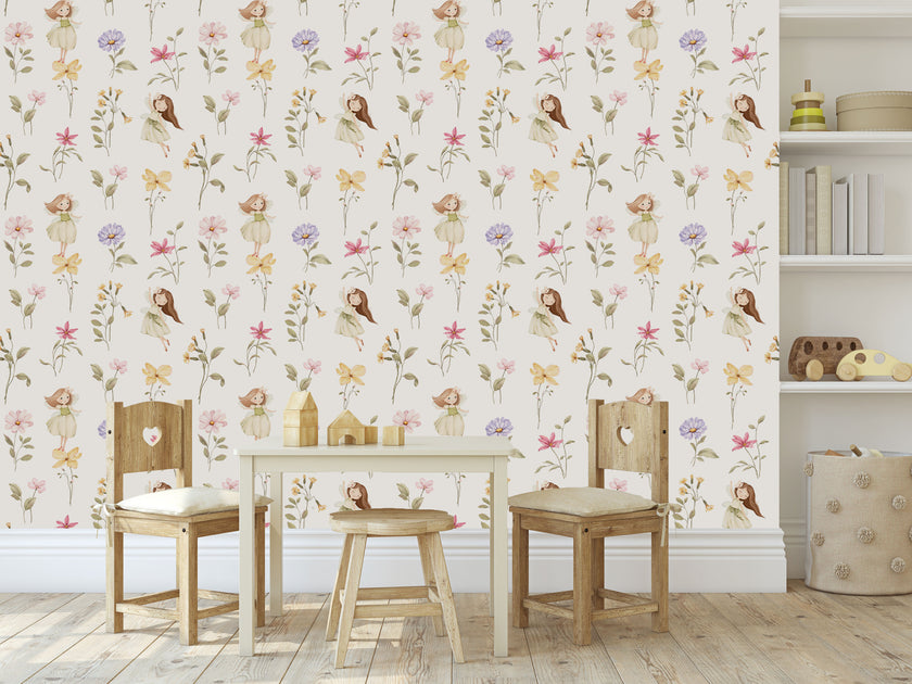 A styled children's playroom featuring a Whimsical little fairy wallpaper with delicate pink, lilac and yellow wildflowers and soft green foliage. In front of the wall is a small wooden table, two wooden chairs with cream cushions, and a small stool.