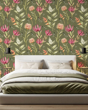 A styled bedroom scene featuring a bed with white and olive bedding in front of a wall covered in a botanical wallpaper with a seamless repeating pattern of hand painted South African fynbos flowers and foliage in blush pink, olive green, and soft neutral tones on an olive background.

