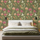 A styled bedroom scene featuring a bed with white and olive bedding in front of a wall covered in a botanical wallpaper with a seamless repeating pattern of hand painted South African fynbos flowers and foliage in blush pink, olive green, and soft neutral tones on an olive background.

