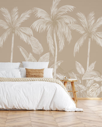 Neutral tropical mural with illustrated palm trees and layered jungle foliage in warm beige and cream inverted tones. On wall behind the bed in white sheets with wooden stool side tables. 