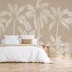 Neutral tropical mural with illustrated palm trees and layered jungle foliage in warm beige and cream inverted tones. On wall behind the bed in white sheets with wooden stool side tables. 