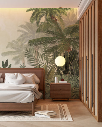 A styled bedroom interior featuring a tropical mural with layered palm trees and lush green foliage on a soft neutral background on the back wall, a wooden bed with white bedding, a matching wooden nightstand and wardrobe, and a round white pendant light.


