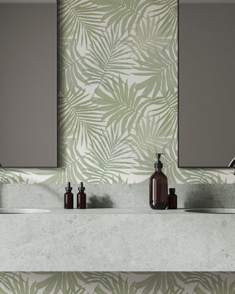 Bathroom featuring Palm Whisper wallpaper with overlapping sage green palm leaves on a white background. The tropical botanical design is displayed behind a double vanity with a marble countertop and two mirrors, creating a fresh coastal inspired space.
