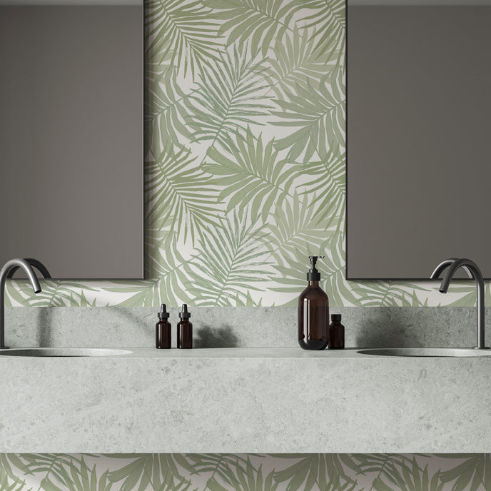 Bathroom featuring Palm Whisper wallpaper with overlapping sage green palm leaves on a white background. The tropical botanical design is displayed behind a double vanity with a marble countertop and two mirrors, creating a fresh coastal inspired space.