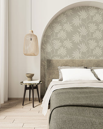 Taupe botanical wallpaper with a seamless repeat, featuring hand-drawn ivory foliage and textured leaves on a warm taupe background. Styled as a feature wall in a curved bedroom alcove behind the bed.