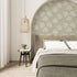 Taupe botanical wallpaper with a seamless repeat, featuring hand-drawn ivory foliage and textured leaves on a warm taupe background. Styled as a feature wall in a curved bedroom alcove behind the bed.
