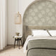 Taupe botanical wallpaper with a seamless repeat, featuring hand-drawn ivory foliage and textured leaves on a warm taupe background. Styled as a feature wall in a curved bedroom alcove behind the bed.