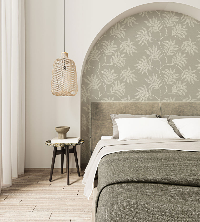Taupe botanical wallpaper with a seamless repeat, featuring hand-drawn ivory foliage and textured leaves on a warm taupe background. Styled as a feature wall in a curved bedroom alcove behind the bed.