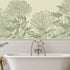 A bathroom scene featuring a white freestanding bathtub with a brass faucet, set against a wall with white subway tiles and a large botanical mural of hand drawn sage green pincushion proteas on a warm ivory background.