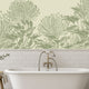 A bathroom scene featuring a white freestanding bathtub with a brass faucet, set against a wall with white subway tiles and a large botanical mural of hand drawn sage green pincushion proteas on a warm ivory background.