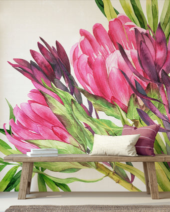 Hand painted watercolour mural featuring vibrant pink proteas with green leaves on a white background. Shown in a styled interior with a wooden bench and pillows.