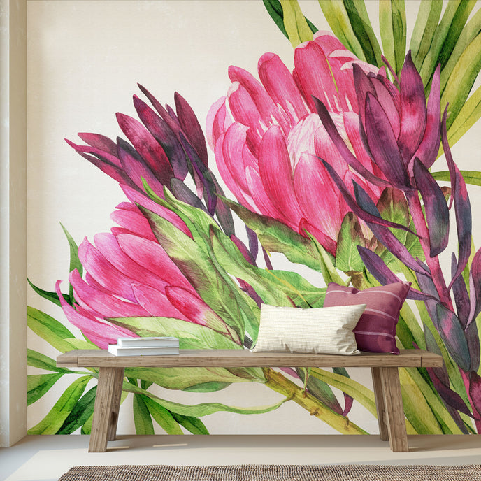 Hand painted watercolour mural featuring vibrant pink proteas with green leaves on a white background. Shown in a styled interior with a wooden bench and pillows.
