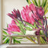 Hand painted watercolour mural featuring vibrant pink proteas with green leaves on a white background. Shown in a styled interior with a wooden bench and pillows.